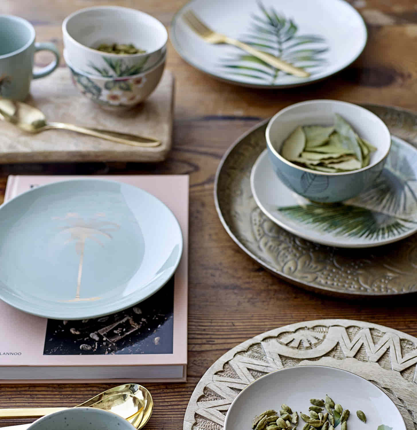 Motivbild zu Bloomingville Aruba Müslischale Blumenmuster: ein brauner Tisch mit verschiedenen Bloomingville Schalen und Teller und einem Buch